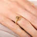 Gold ring with a brown diamond on a person's finger against a neutral background