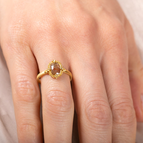 Gold ring with a brown diamond on a person's finger against a neutral background