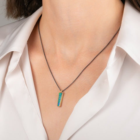 Handcrafted necklace featuring an Australian opal doublet stone set in a gold bezel and paired with an oxidized silver chain, worn on a person's neck.