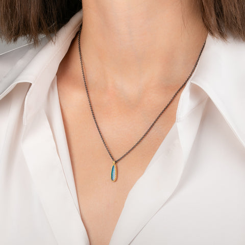 Handmade necklace featuring an Australian opal doublet stone set in an 18k gold bezel and paired with an oxidized silver chain worn on a model's neck.