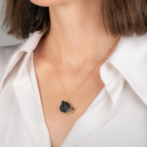 Gold necklace featuring a jasper gemstone carved into a black bear face worn on a model's neck.