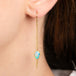 A gold drop earring with a teardrop-shaped black opal stones, hanging from a delicate chains, shown worn on a model's ear.