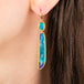 Close up of a gold dangle earring with oval and elongated black opal gemstones, worn on a person's ear.