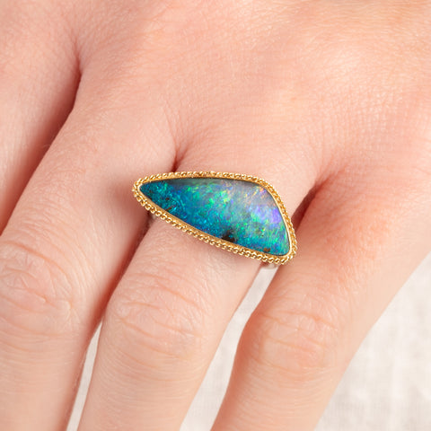Close up of a person wearing a handmade fine jewelry boulder opal ring with an 18k gold bezel and sterling silver band