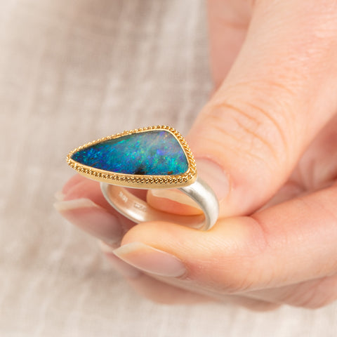 Close up of a person holding a handmade fine jewelry boulder opal ring with an 18k gold bezel and sterling silver band