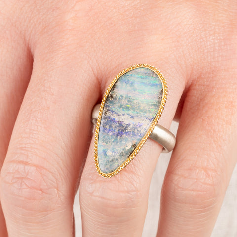 Close up of a person wearing a handmade fine jewelry boulder opal ring with an 18k gold bezel and sterling silver band