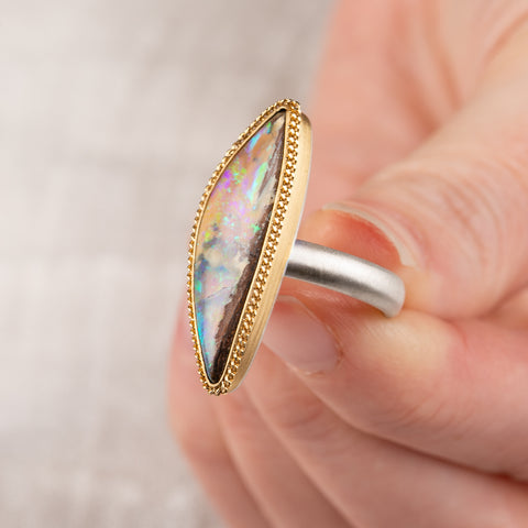 Hand holding a boulder opal ring with 18k gold bezel and sterling silver band