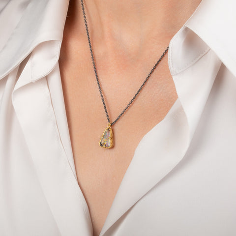 A necklace featuring a boulder opal set in an 18k gold bezel and suspended from an oxidized silver chain, worn on a person's neck.