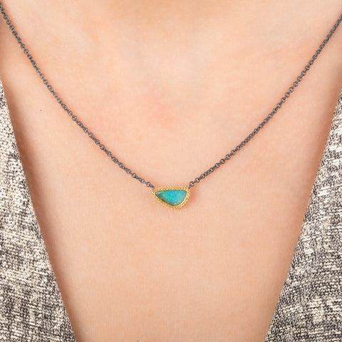 Handmade necklace featuring a boulder opal stone set in an 18k gold bezel and paired with an oxidized silver chain, worn on a person's neck.