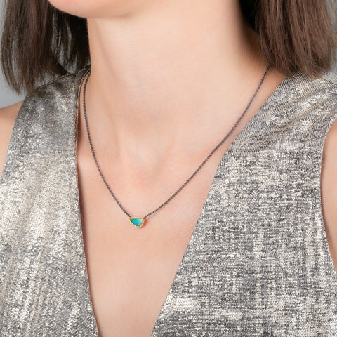 Handmade necklace featuring a boulder opal stone set in an 18k gold bezel and paired with an oxidized silver chain, worn on a person's neck.