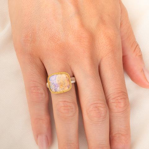 Handmade ring featuring a boulder opal gemstone set in an 18k gold bezel and paired with a sterling silver band, worn on a person's finger.