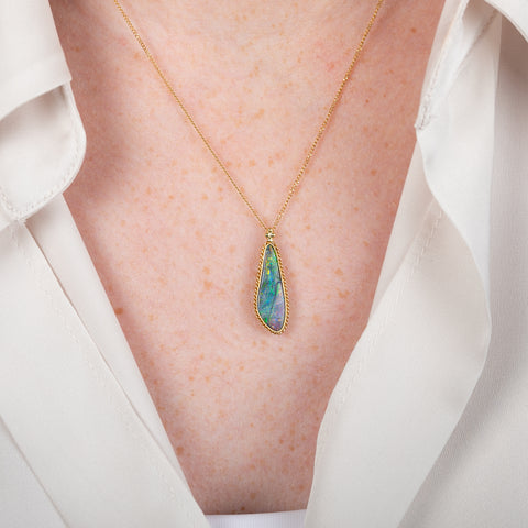 Boulder opal pendant necklace in a gold bezel on a person