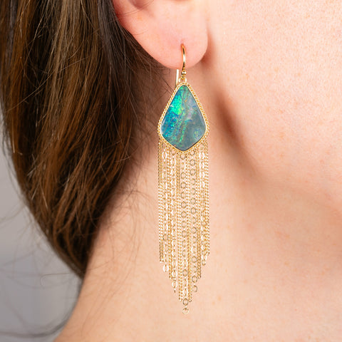 Gold fringe earring with a boulder opal gemstone worn by a person.