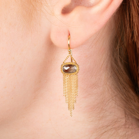 Gold earrings featuring brown diamonds and gold chain tassels, shown worn in a person's ear.