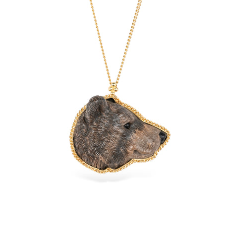 Hand-carved bear head pendant set in an 18k gold bezel, on a gold chain against a white background.