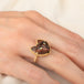 A gold ring featuring a carved dark brown and black cat face with green Tourmaline eyes, worn on a person's finger.