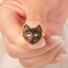 A gold ring featuring a carved dark brown and black cat face with green Tourmaline eyes, held in hand.