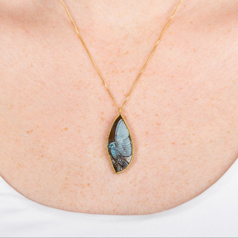 Carved phoenix boulder opal necklace in a gold setting worn on a person