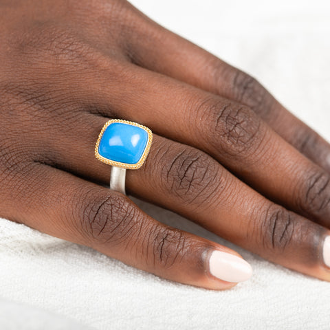 Gold and silver ring with blue ceruleite stone on a person's finger.