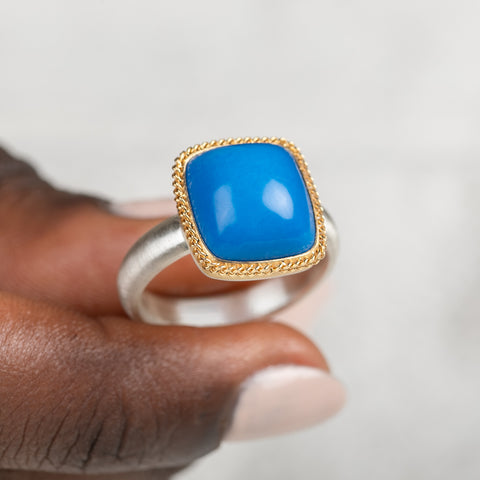 Gold and silver ring with blue ceruleite stone held in a person's hand on a white background