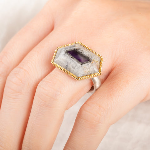 A close up of a person wearing a handmade fine jewelry amethyst gemstone ring set in 18k gold with a sterling silver band