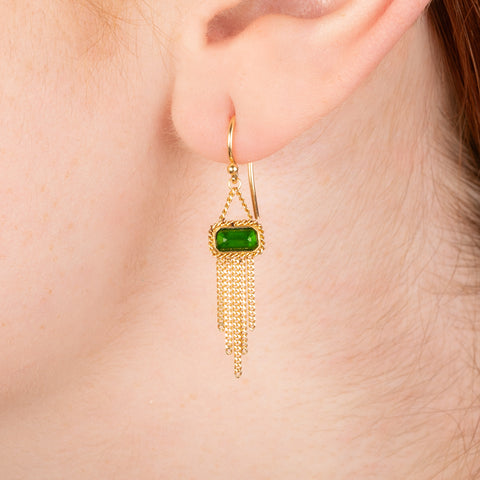 Gold earrings featuring chrome diopside gemstones and gold chain tassels, shown worn in a person's ear.