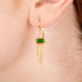 Gold earrings featuring chrome diopside gemstones and gold chain tassels, shown worn in a person's ear.