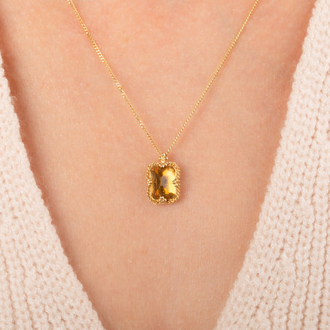 Gold necklace featuring a citrine gemstone worn on a person's neck.
