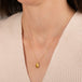 Gold necklace featuring a citrine gemstone worn on a person's neck.