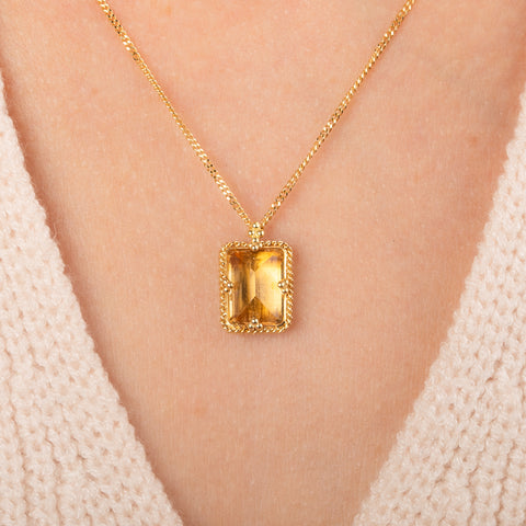 Gold necklace featuring a rectangular citrine gemstone, worn on a person's neck.