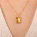 Gold necklace featuring a rectangular citrine gemstone, worn on a person's neck.