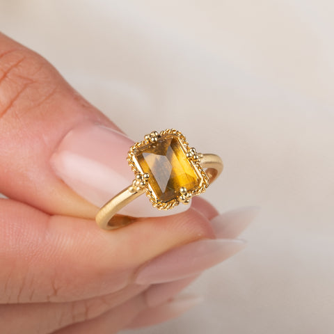 Gold ring featuring a citrine stone set in an 18k gold bezel, held in a hand.