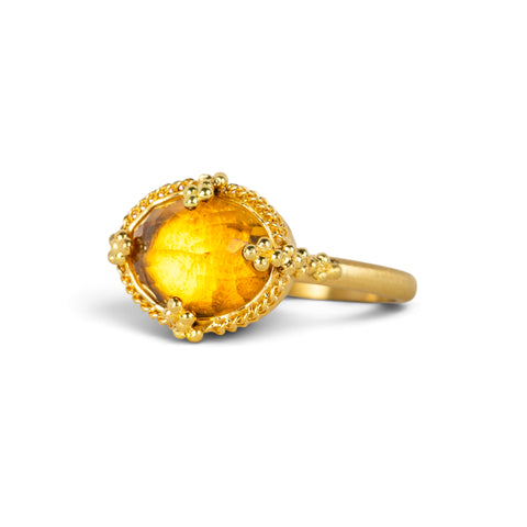 A gold ring featuring a citrine gemstone, set against a white backdrop. 
