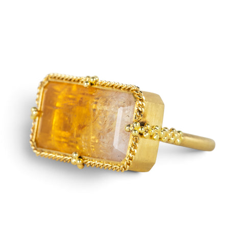 A gold ring featuring a large, rectangular, Citrine gemstone set in a detailed gold bezel, seen against a white background.