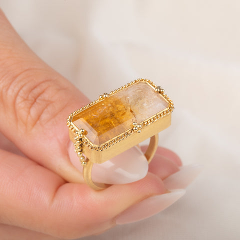A gold ring featuring a large, rectangular, Citrine gemstone set in a detailed gold bezel, held in hand.