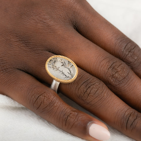 Gold and silver ring featuring a dendritic quartz stone on a person's hand