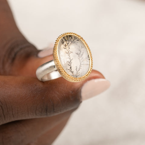 Gold and silver ring featuring a dendritic quartz stone held in hand