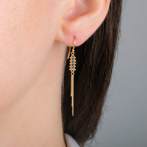 Close up of a gold tassel earring featuring a row of four champagne diamonds, worn in a person's ear.
