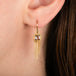 A gold dangle earring with square diamond and gold chain tassel, shown worn on a person's ear.