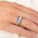 An oval ring featuring a textured light blue dumortierite stone in a yellow gold bezel setting and a matching gold band, worn on a person's finger.