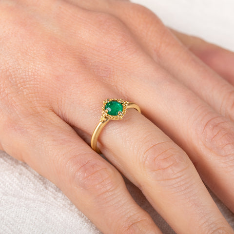 Gold ring with an emerald gemstone on a person's finger against a neutral background