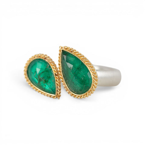 A gold and silver ring featuring two emerald stones against a white background
