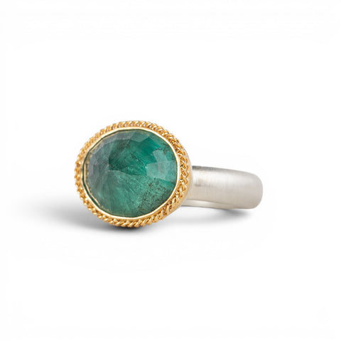 An oval emerald gemstone ring set in a gold bezel, with a sterling silver band, shown against a plain white background.