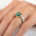 An oval emerald gemstone ring set in a gold bezel, with a sterling silver band, on a finger