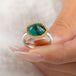 An oval emerald gemstone ring set in a gold bezel, with a sterling silver band, held in hand.
