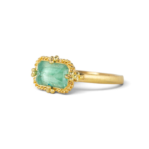 A gold ring featuring a light green emerald gemstone, against a white background.