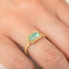 A gold ring featuring a light green emerald gemstone, worn on a person's finger.