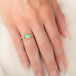 A gold ring featuring a light green emerald gemstone, worn on a person's finger.