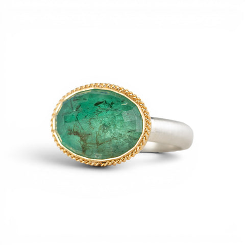 A gold and silver ring featuring an emerald stone, shown against a white background.