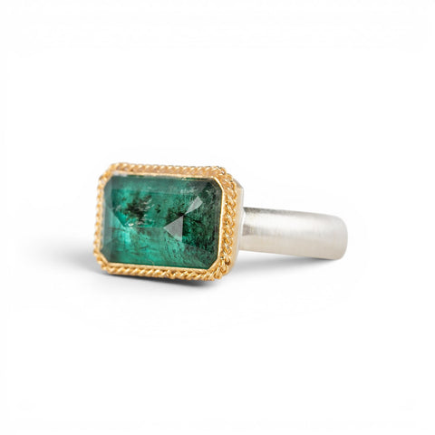 A rectangular emerald stone ring with a gold bezel and a sterling silver band, shown on a plain white background.